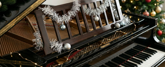 Grand piano music stand decorated with silver tinsel and blue ornaments for an improvers level Deck the Halls piano lesson with free sheet music.